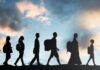 Integrating adult refugee students Silhouettes of seven people of various ages walking with backpacks against a cloudy sky at sunset.