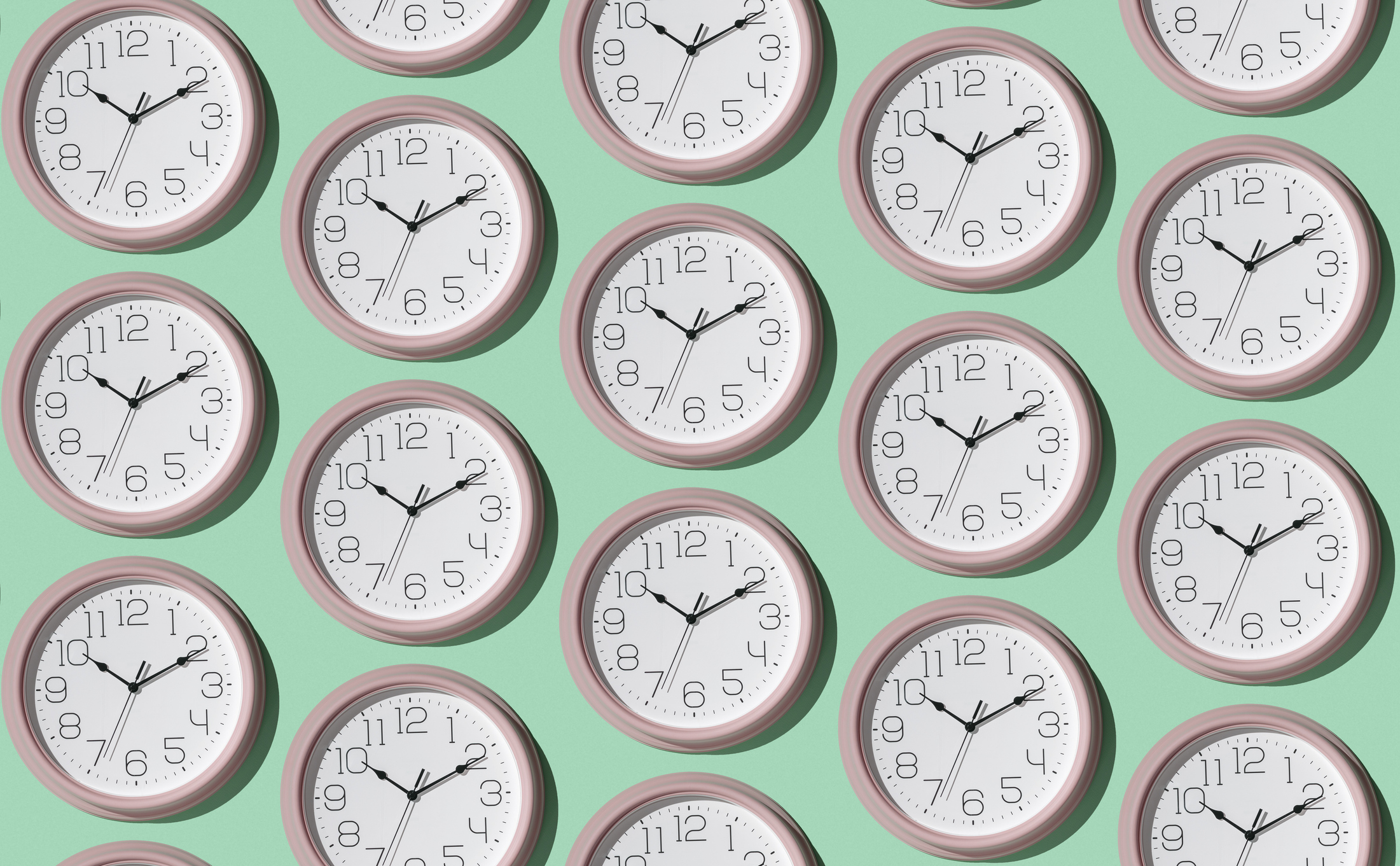 A pattern of analogue clocks with pink frames and white faces, each showing different times, set against a mint green background.