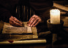 Why learning to write is far more challenging than reading A person's hands writing on parchment with a quill pen, illuminated by candlelight, alongside an ancient book.