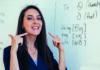 Supercharge your course material with pronunciation A woman stands in front of a whiteboard, pointing to her mouth while teaching pronunciation. The whiteboard displays phonetic symbols and words like 'thing' and 'with' with their phonetic transcriptions.