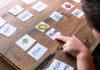 Visualising pronunciation A child points to a card labeled 'YELLOW' with a drawing of a yellow object, amid other flashcards with drawings and labels like 'HORSE,' 'MOON,' 'FISH,' and colors on a wooden table.