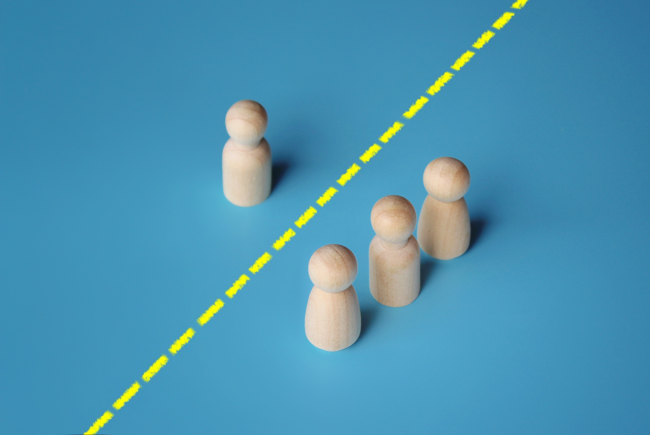 Four wooden figurines on a blue surface, with three grouped together on one side of a yellow dashed line and one isolated on the other side.
