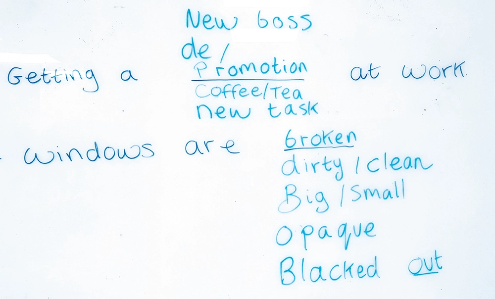 A whiteboard with phrases written in blue marker, including: "Getting a new boss", "de/promotion", "Coffee/Tea", "new task at work", "windows are broken", "dirty/clean", "big/small", "opaque", and "blacked out".