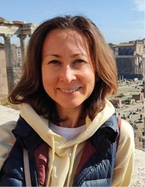 A woman smiling with ancient ruins in the background on a sunny day.