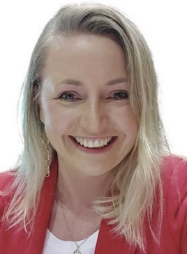 A person smiling, wearing a red blazer and white top, with shoulder-length blonde hair.