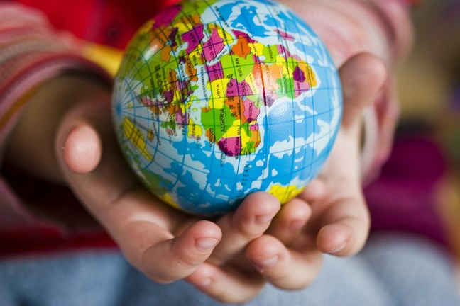 A small globe held in the hands of a child, showing a colourful map of the world.