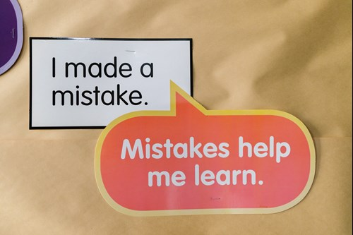 Two signs on a wall; one says 'I made a mistake.' and the other says 'Mistakes help me learn.' in a speech bubble format.