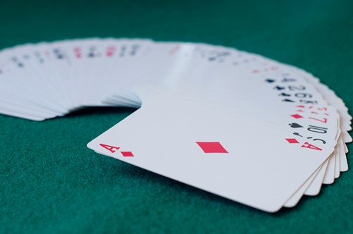 A deck of playing cards fanned out on a green table, with the Ace of Diamonds prominently visible in the foreground.
