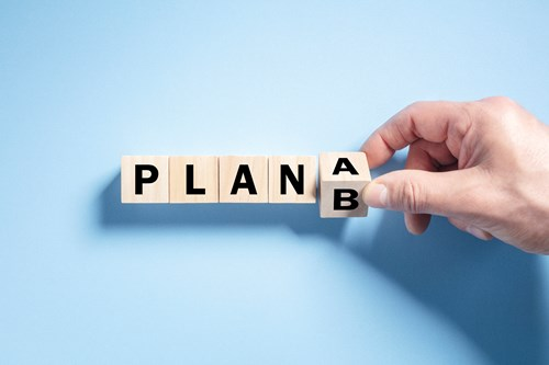 A hand arranging wooden blocks with letters to spell out 'PLAN B' against a blue background.