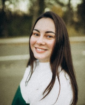 A woman with long dark hair and a white sweater smiling at the camera outdoors.