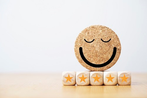 A cork coaster with a smiley face drawn on it, placed on top of five wooden blocks, each featuring a golden star, representing a five-star rating.