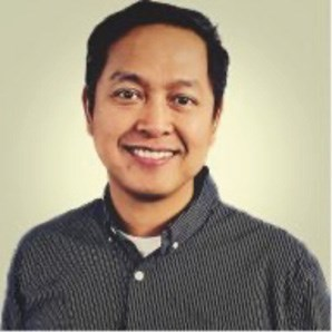A man wearing a dark, striped button-up shirt smiles at the camera against a plain background.