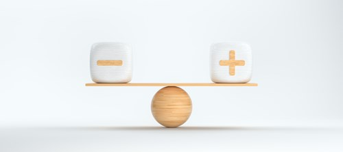 A balancing scale with a wooden sphere as the pivot, a plank on top, and a cube with a minus sign on the left and a cube with a plus sign on the right.