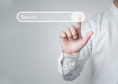 A person in a white shirt is touching a virtual search bar with their index finger, set against a plain background.
