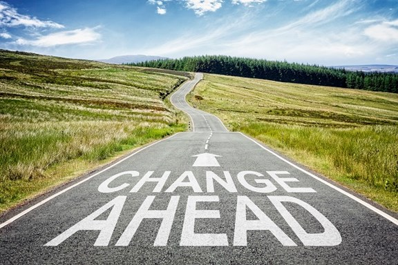 A straight road running through a grassy landscape with forests in the distance, featuring the words 