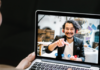 Building bridges between class and online students A person sitting on a sofa is having a video call on a laptop with a man who is smiling and gesturing with his hand.