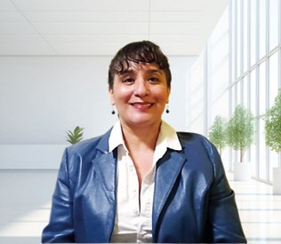 Person wearing a blue blazer and white shirt, smiling while sitting in a well-lit room with large windows and plants.