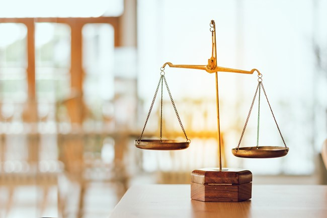 A brass balance scale placed on a wooden surface with a blurred background of a bright room.