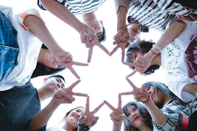 A group of people forming a star shape with their hands, viewed from below against a clear sky.