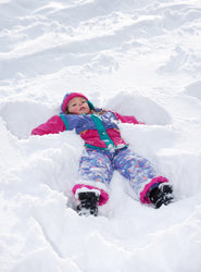A child wearing colourful winter clothing lying on their back in the snow, making a snow angel with arms and legs outstretched.