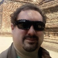 A person wearing sunglasses standing in front of a brick wall structure.