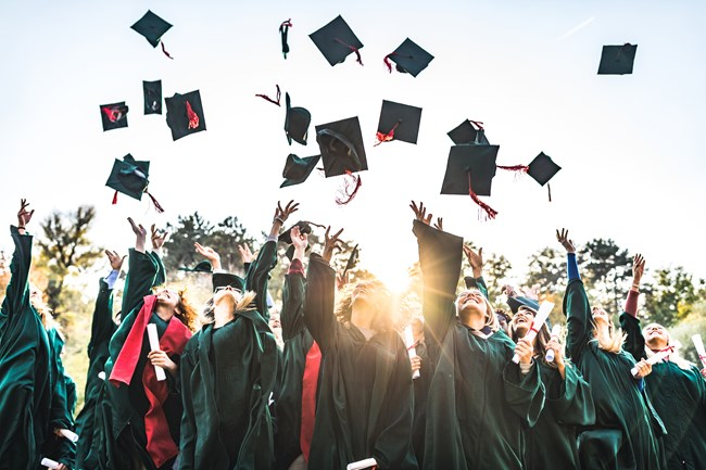 Group of graduates in caps and gowns cheerfully throwing their graduation caps into the air outdoors, celebrating their achievement.