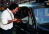 Identity and the English classroom A man holding a wallet is speaking to a taxi driver through the passenger window of a black taxi on a city street in the evening.