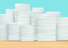 Low paper – high interest Stacks of white paper piled high on a wooden surface against a light blue background.