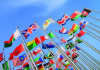 Building a multinational tutor team Multiple flags from different countries waving on flagpoles against a clear blue sky.
