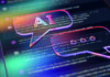 When AI meets the classroom A digital illustration featuring two holographic speech bubbles overlaid on computer code. One bubble contains the letters "AI" while the other shows ellipses, suggesting an ongoing conversation or dialogue. The image is enhanced with vibrant, neon colours, creating a futuristic and dynamic atmosphere.