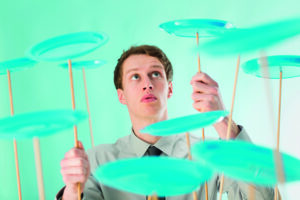 A person skillfully balances multiple green spinning plates on wooden sticks, concentrating on maintaining their spin, against a green background.