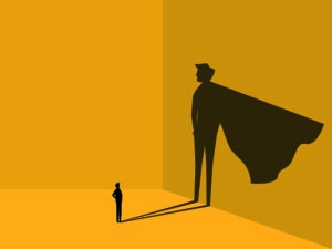 A small figure stands confidently with arms crossed, casting a large shadow on the wall resembling a superhero with a cape, in a minimalist style with a warm yellow background.
