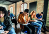 Give writing a chance A diverse group of students seated in a classroom with brick walls, concentrating on writing in notebooks at their desks.