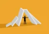 Barriers to change Illustration of a silhouetted figure standing under a collapsing row of large white dominoes on an orange background.