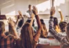 Methods, myths and mindfulness Students in a classroom raise their hands while seated at desks, listening to a teacher at the front of the room.