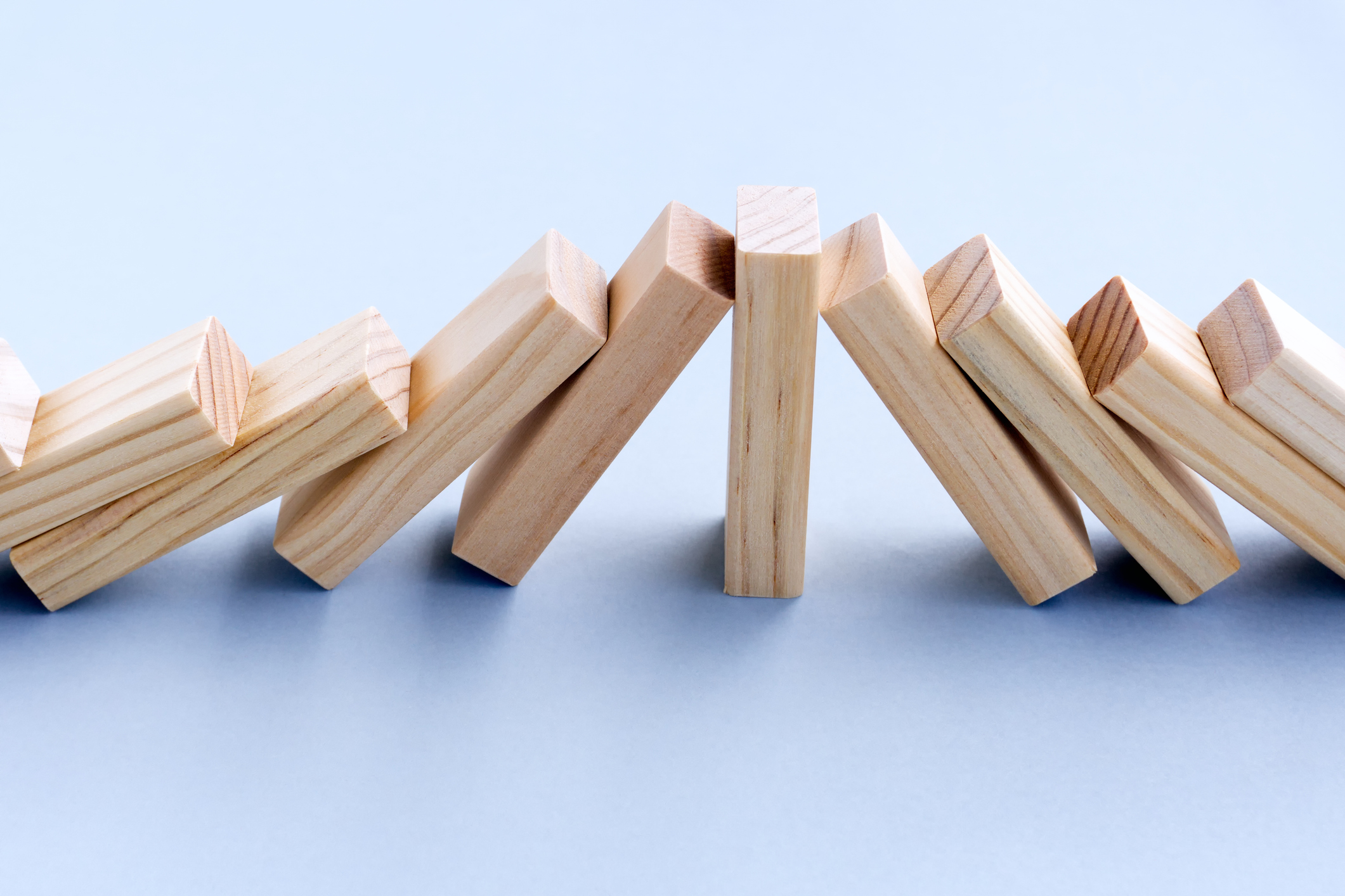 A row of wooden dominoes falling over on a light blue background.