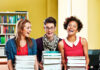 Choosing a course book – What checklists don’t tell you Choosing a course book – What checklists don’t tell you - Three young adults sitting in a library, each holding a stack of books and smiling widely, with bookshelves in the background.
