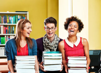 Choosing a course book – What checklists don’t tell you Choosing a course book – What checklists don’t tell you - Three young adults sitting in a library, each holding a stack of books and smiling widely, with bookshelves in the background.