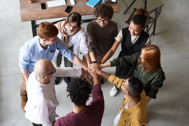 A group of people standing in a circle with their hands joined together in the center, symbolizing teamwork and unity.