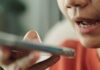 Speaking personally Close-up of a person speaking into a smartphone, holding it near their mouth, suggesting the use of a voice assistant or recording app.