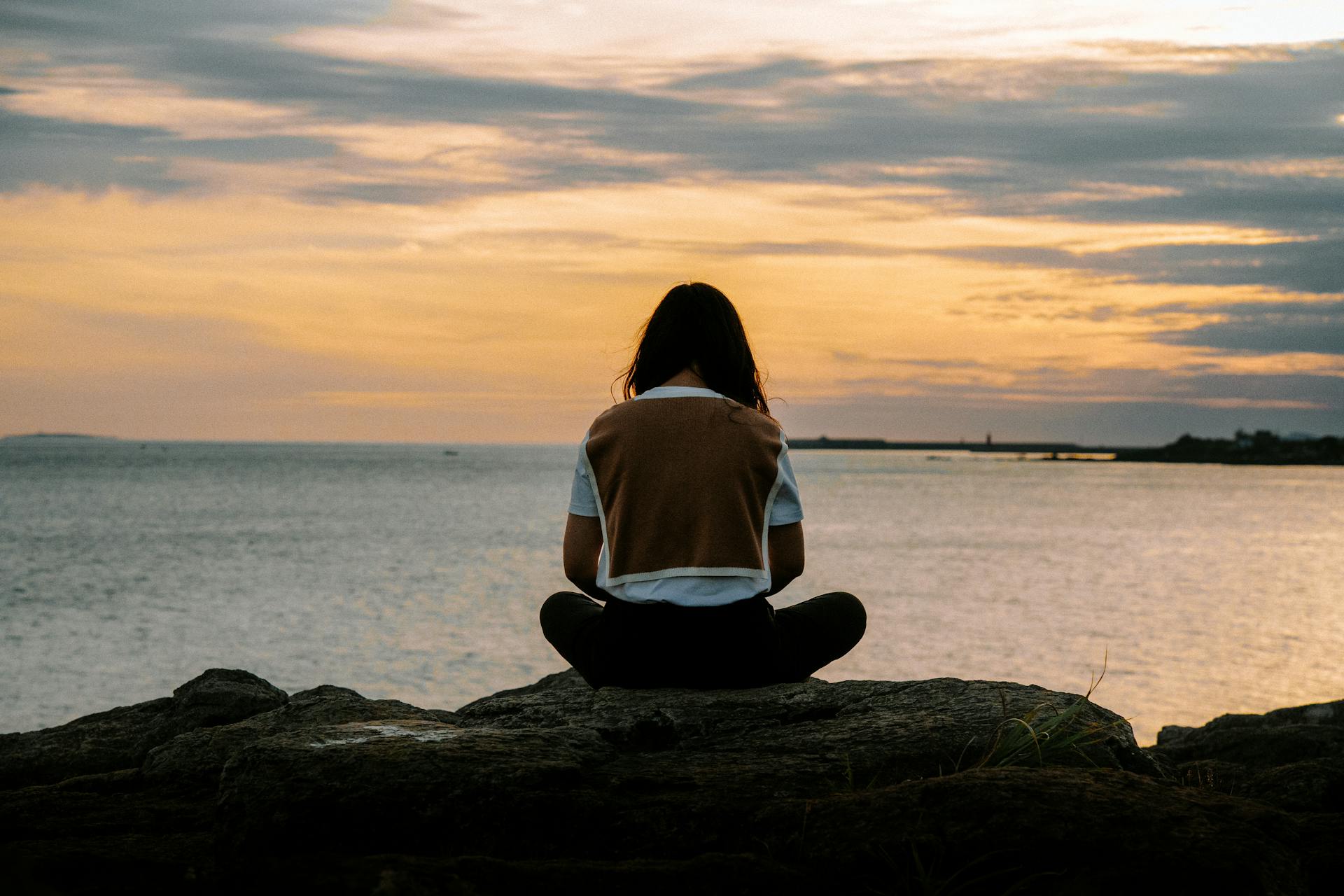 young person sitting on rocks at sunset